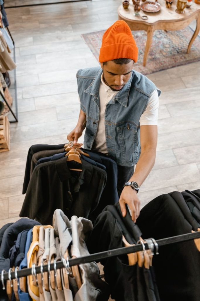 Crafting Captivating Headlines: Your awesome post title goes here Man examines clothing in boutique wearing denim vest and orange beanie.